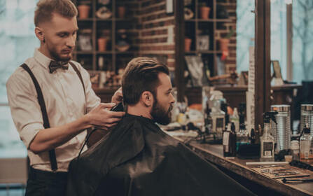 Barber trimming a client’s beard with clippers in a barber chair