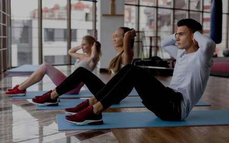 Three people performing sit-ups together on mats in a fitness studio
